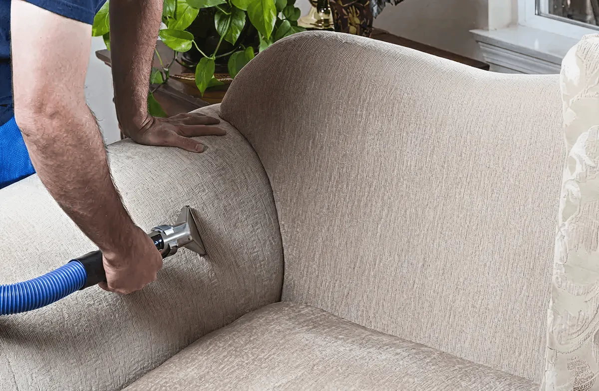 Professional upholstery cleaner deep-cleaning a fabric sofa with a handheld extraction tool and hose, Charlotte, NC.